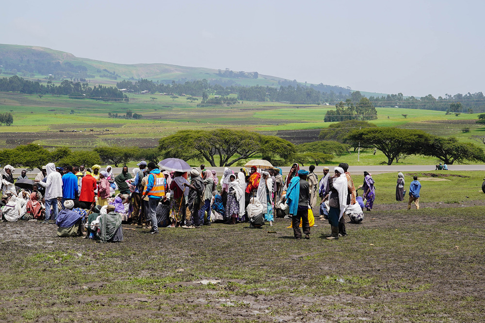 A group of internally displaced people wait on an arid landscape to receive aid in the town of Dabat.