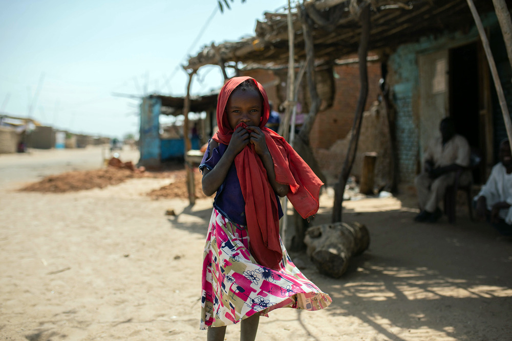 A young child stands in a dusty street, looking at the camera
