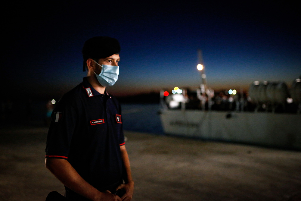 A policeman stands guard near a quarantine ferry in Italy at night.