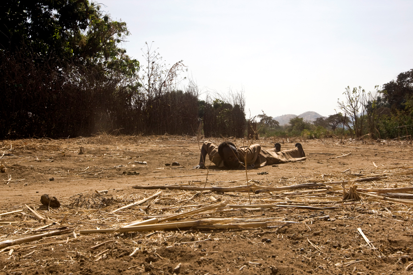 A man is laying on the ground as a Government Antonov plane is bombing Kauda Town
