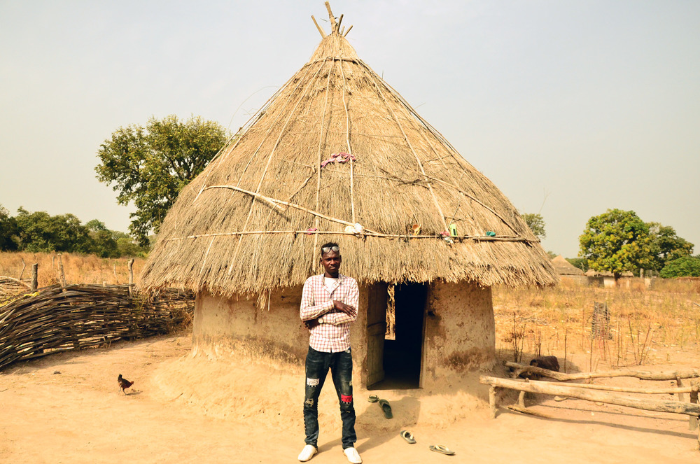 Ousmane Diallo stands in front of a thatched roof home in his village of Pakour, Senegal