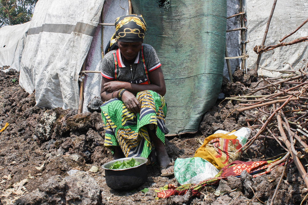 A woman bends over in front of a temporary shelter.