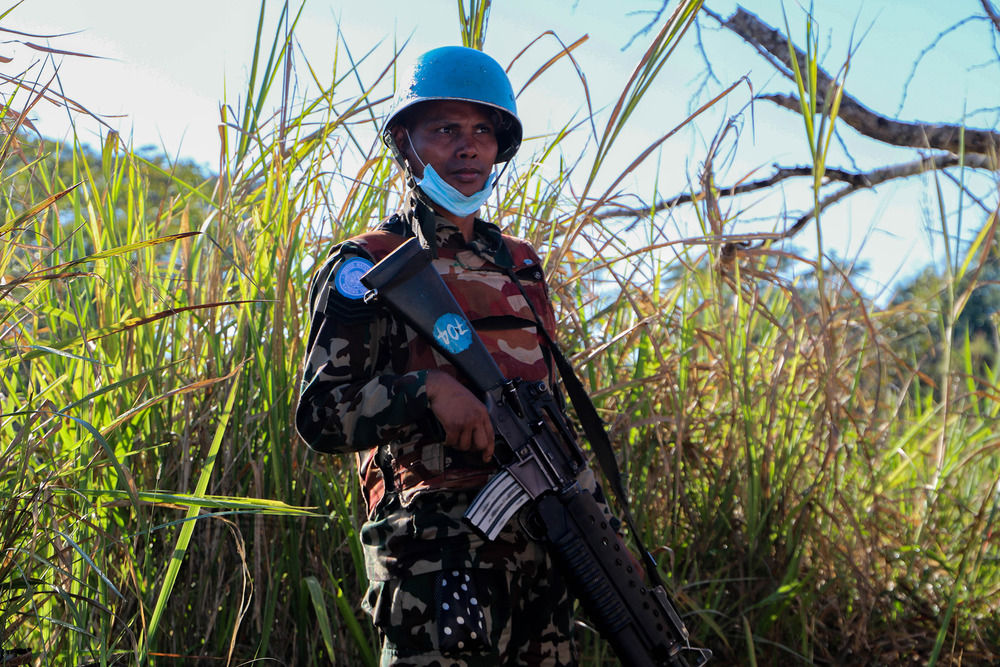 A UN peacekeeper holds a gun standing in front of a field of tall grass.