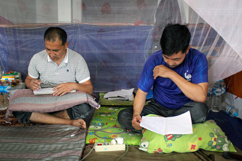 Two men sit cross-legged on the ground while reading books.