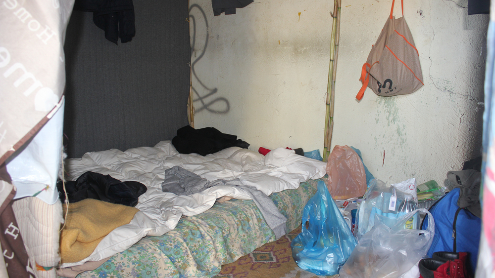 An abandoned crumbling outhouse, without any windows or capacity for natural light except through the cracks in the ceiling, has become a living space for about 100 people in Pyli.