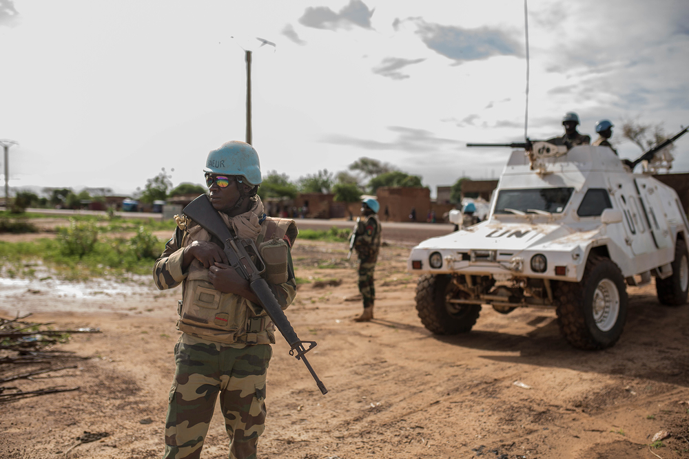A UN peacekeeper with a gun looking out in front of a UN tank