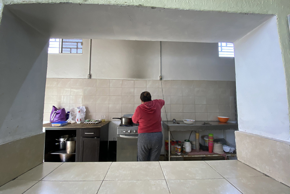 A woman cooks over a stove through an alcove of a building with her back to the camera.