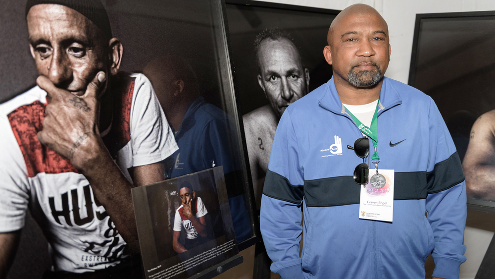 Pastor Craven Engel stands next to portraits of “interrupters”. He uses former gangsters as mediators and negotiators to reduce gang violence in Hanover Park.