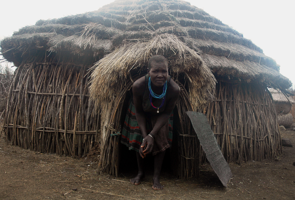Photo of a woman in Uganda exiting a thatched house.