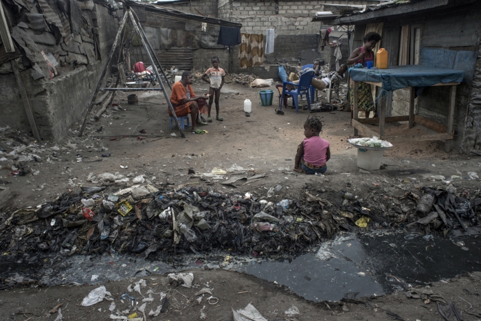 A child sits by the rising tide of faeces and organic waste near her home