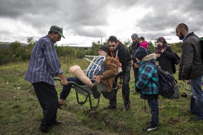 Disabled man carried over the bumpy ground to the border