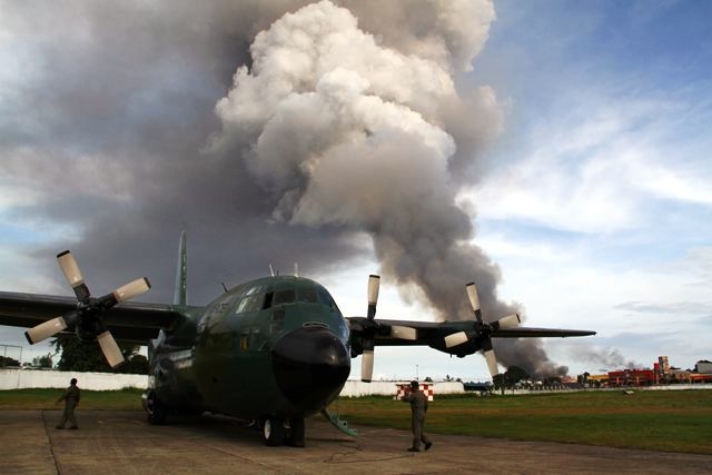Zamboanga, Philippines - Black smoke from burning houses rises in the background as a military cargo plane bearing relief goods arrives in the besieged city of Zamboanga in Mindanao, where troops are locked in a battle with Muslim rebels opposed to peace