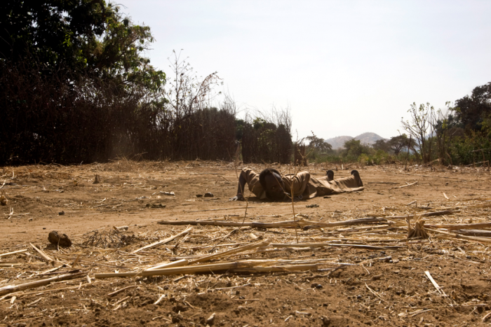 A man is laying on the ground as a Government Antonov plane is bombing Kauda Town