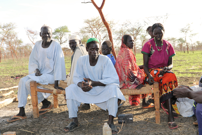Noor Faki sits on a bed in his yard with his neighbours in South Ulu village.
