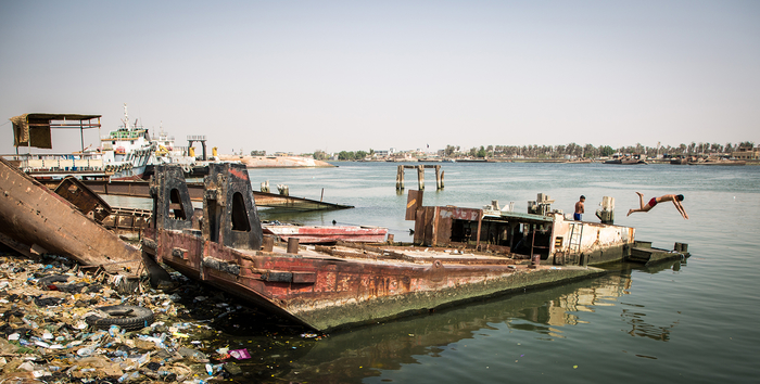 Young man diving from a wrecked ship into the polluted Shatt al-Arab river in Basra.