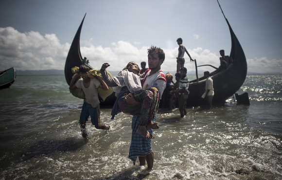 A Bangladeshi man helps Rohingya Muslim refugees to disembark from a boat on the Bangladeshi shoreline of the Naf river after crossing the border from Myanmar in Teknaf on 30 September 2017.