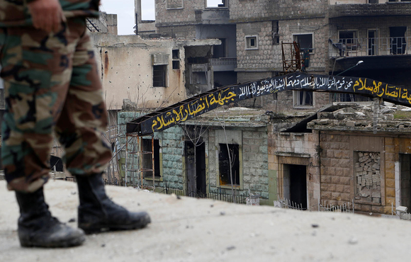 A Syrian army soldier stands on a roof near a street sign that was written by rebels in the streets of Maarat al-Numan, the town taken this week by government forces.