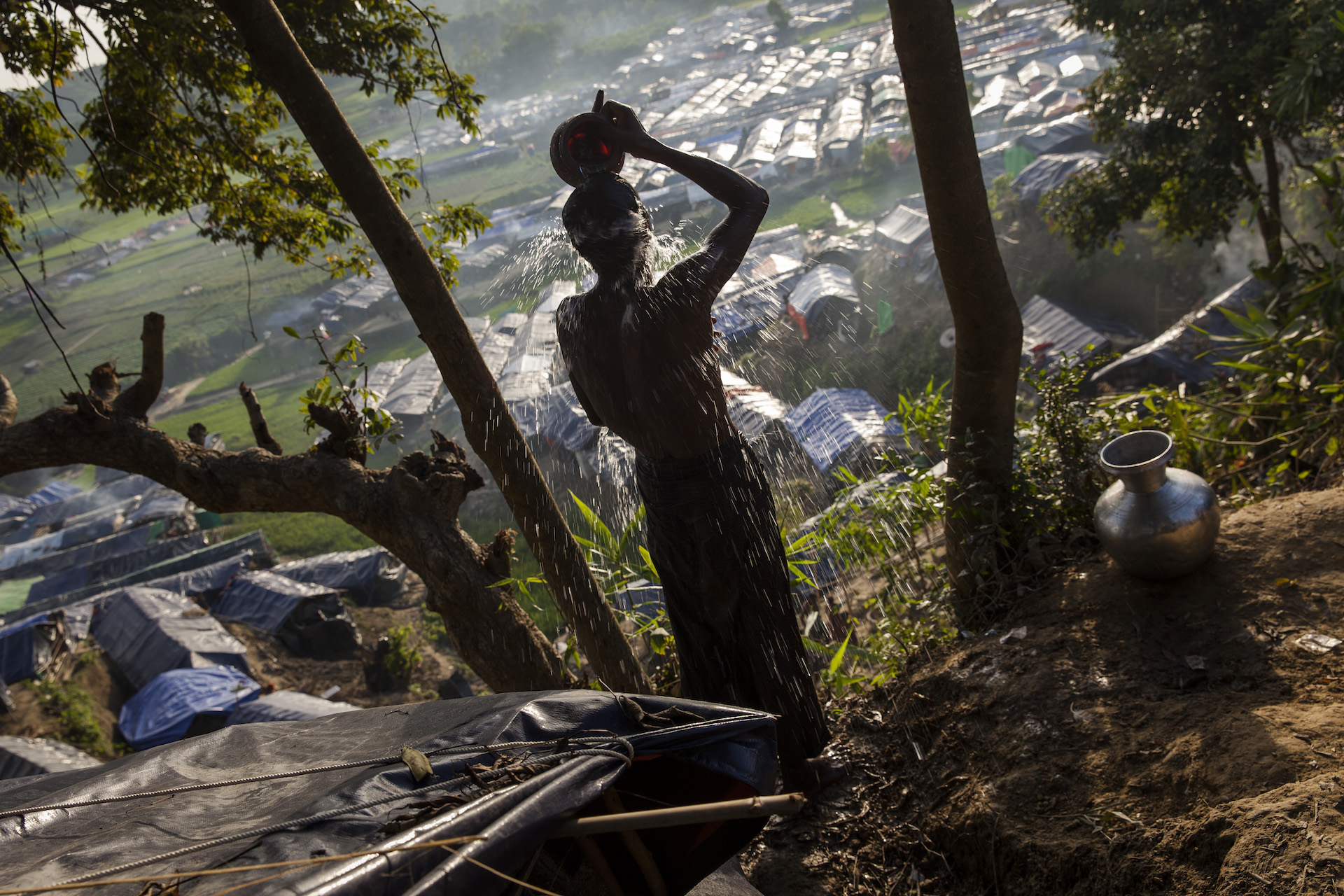 A Rohingya man washes himself on a hill overlooking tarpaulin-covered shelters