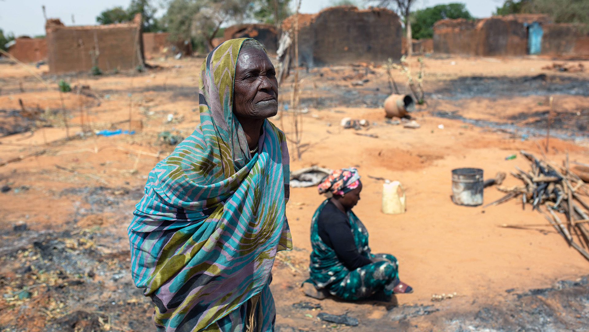 A woman stands in a barren field near a camp.