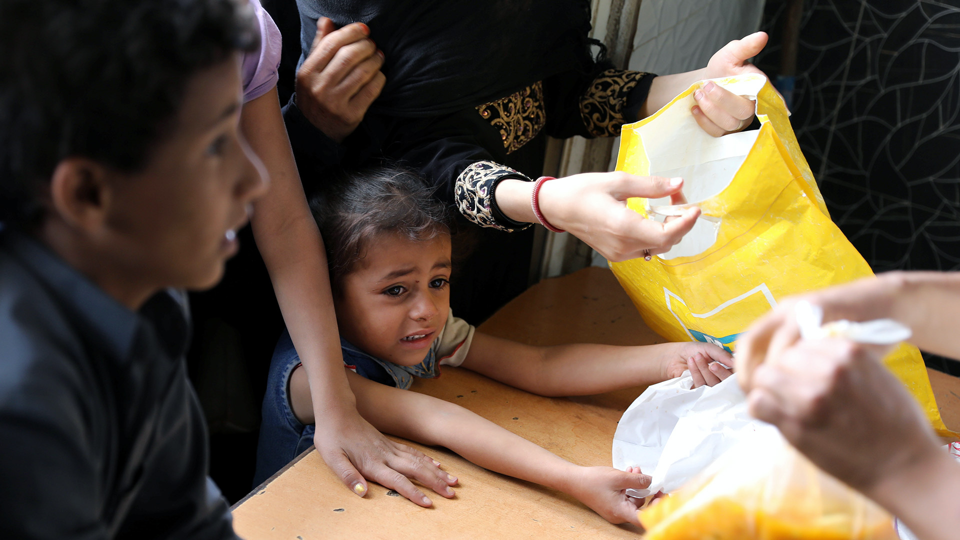A girl looks on as worker gives a food ration to a boy at charity kitchen in Sana'a, Yemen 20 July, 2020