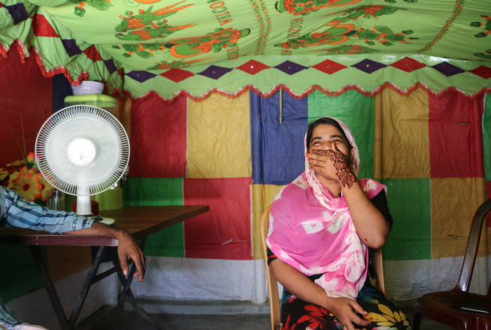 Photo of Romida Begum sitting inside with her hand covering her smiling mouth