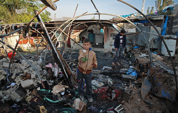 A Syrian boy holds a rose inside a charred tent following Syrian regime bombardment on a makeshift camp in the village of Qah near the Turkish border in the northwestern Idlib province on 21 November 2019.
