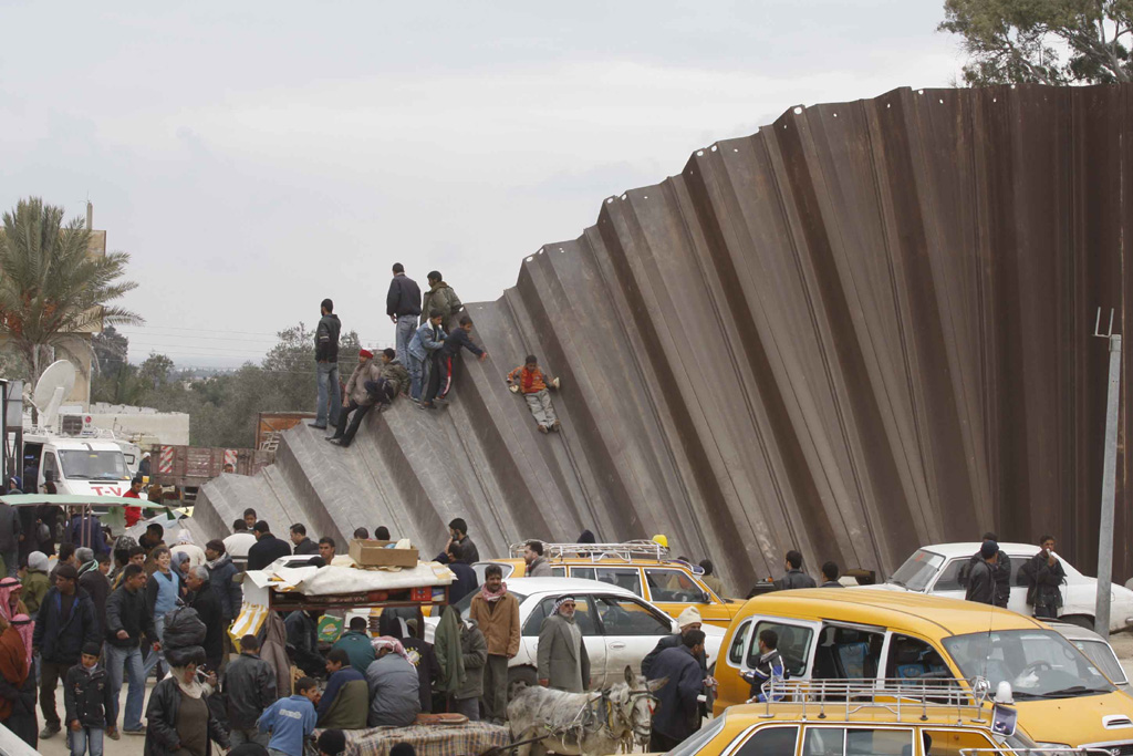 Palestinians cross over a section of the border wall separating the