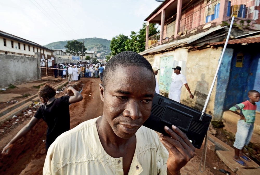 A man listens to the radio as people wait to vote in legislative and presidential elections 17 November 2012 in  Fourah Bay, Freetown