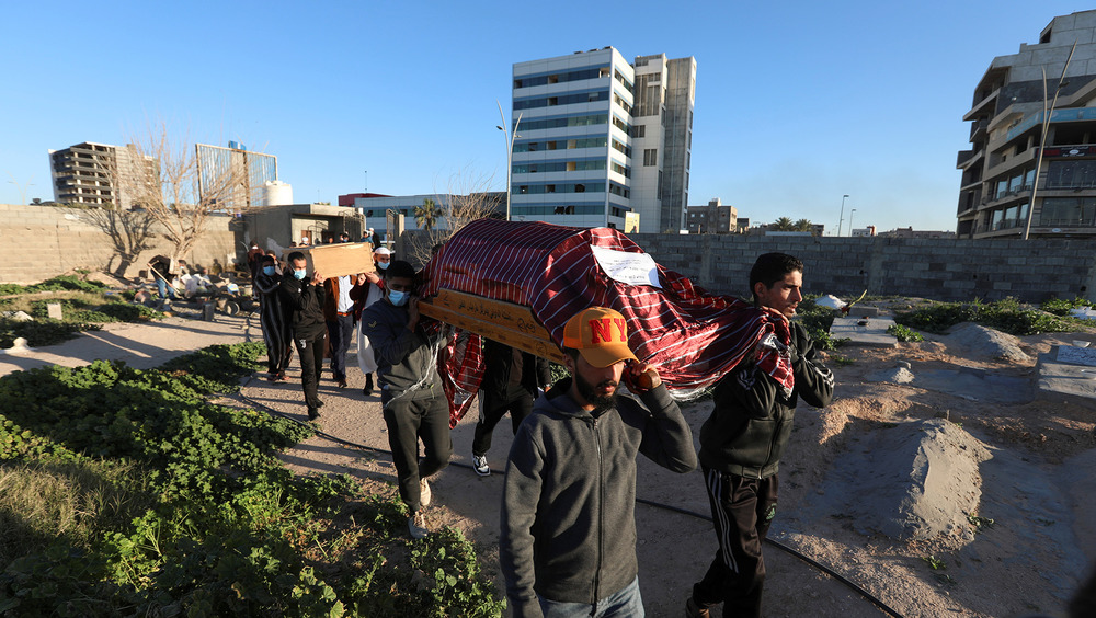 The image shows several men carrying a coffin with the Libya skyline in the background.