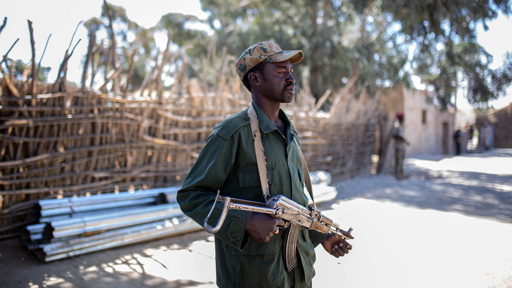 A man stands in a street, holding a gun.