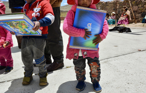 Two children, their faces cropped out of the frame, hold large school books.