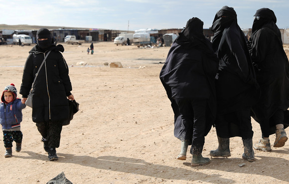 A woman holds hands with a child while walking through al-Hol camp, Syria