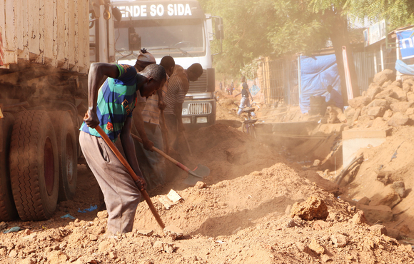 A group of men dig ditches along the main road in Tougan