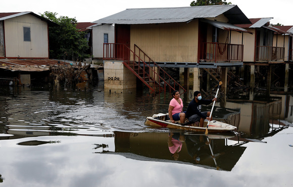People travel through a flooded street on a jet ski hull, the houses in the background are submerged by floodwaters.