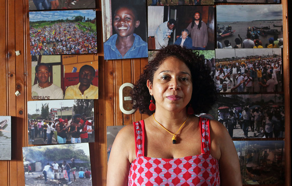 A portrait of  Danelly Estupiñán standing against a wooden wall decorated with photographs 