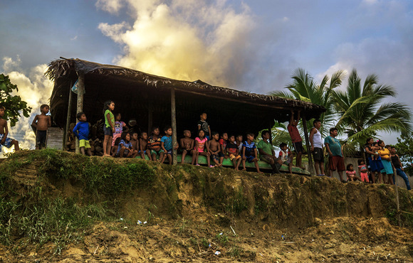 Children and adults stand on the riverbank of Puerto Olave, a community of 300 Indigenous people that has been effectively cut off from the outside world due to conflict.