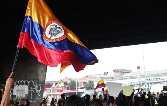 A large Colombian flag waves above a sea of people's heads.