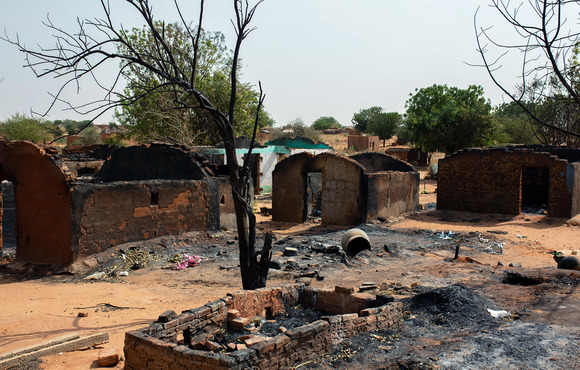 Multiple burnt dwellings stand empty in a dusty village. 