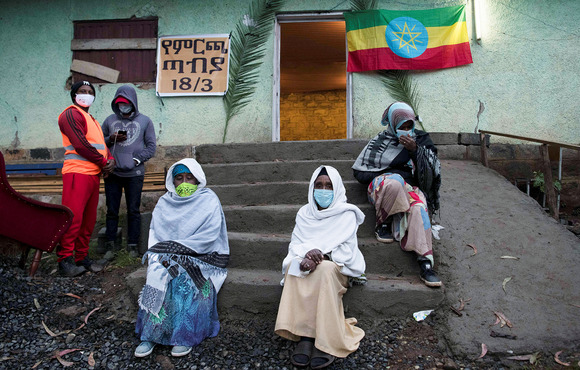 Several people sit on the front steps of a building; an Ethiopian flag hanging on the outside wall.