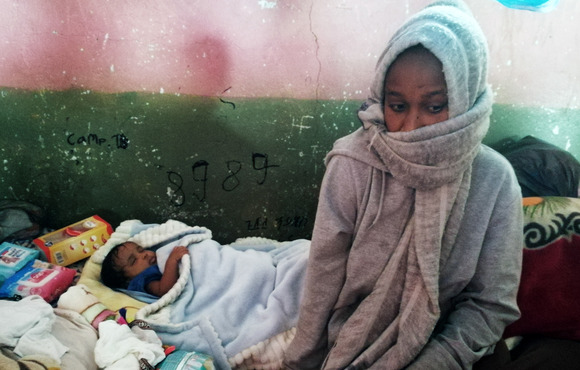 A mother sits in a makeshift shelter next to her sleeping child. 