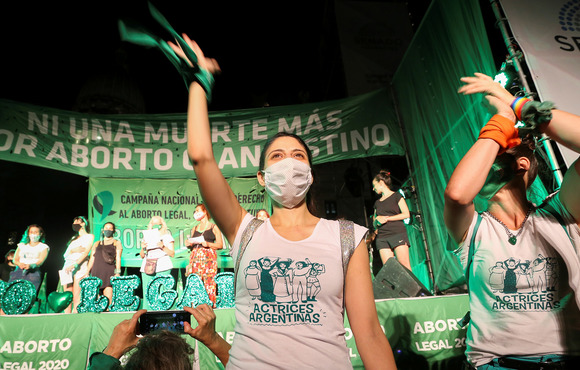 A demonstrator at a pro-abortion rally stands in front of a green banner cheering with one arm up. 