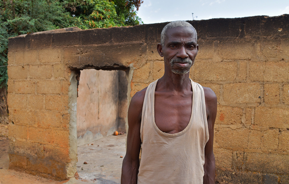 A man stands in front of a burnt out stone house 