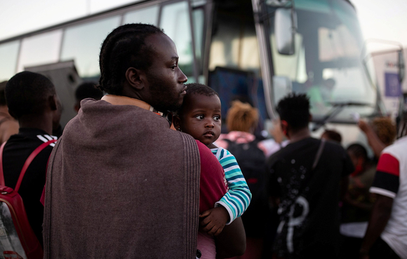 A man holds a child as refugees and migrants wait to board a bus following last month’s fire at the Moria camp on the island of Lesvos, Greece. 