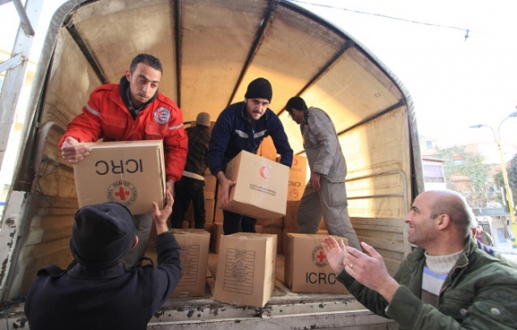 Local people help Syrian Arab Red Crescent volunteers unload food parcels from trucks in the main square of Bludan, Syria, at an impoverished warehouse donated by a local businessman