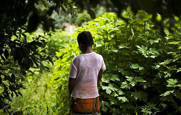 A girl stands in a green space, looking away from the camera.