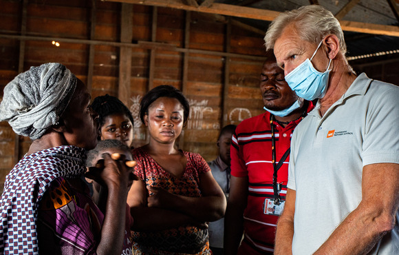 A man in a disposable mask speaks with a woman who wears a headscarf. 