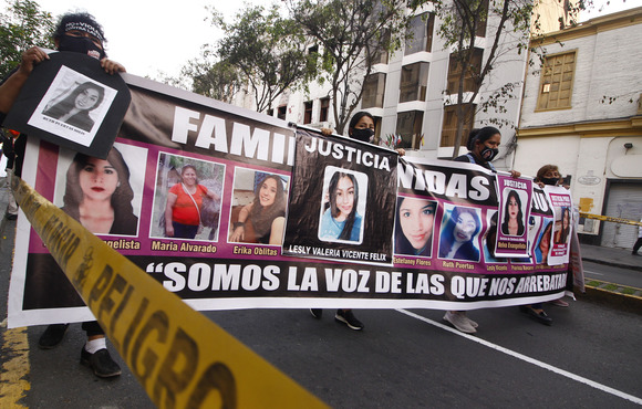 Image shows severl people holding a banner with faces of women and girls as they walk down a street. 