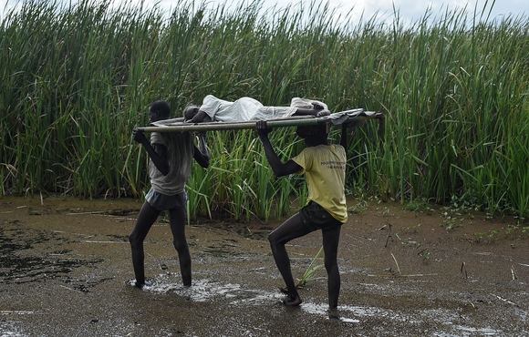 Men carry an elderly woman through the swamps