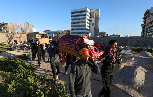 The image shows several men carrying a coffin with the Libya skyline in the background.