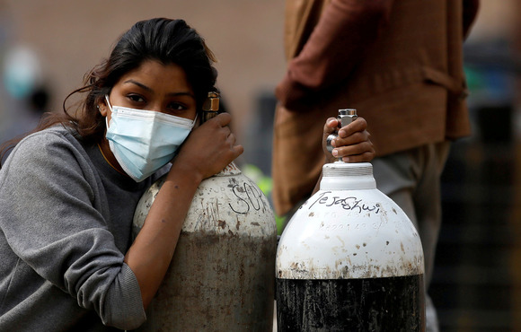 A girl crouches down beside two oxygen tanks, her face covered in a disposable mask. 